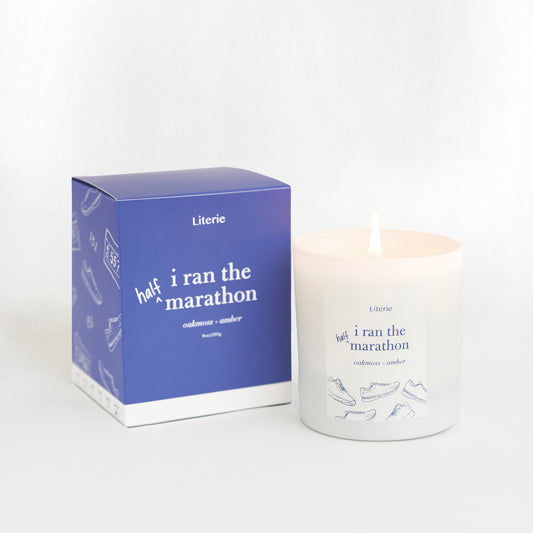 A candle with a label that reads 'half i ran the marathon' next to its packaging box which has a similar design.