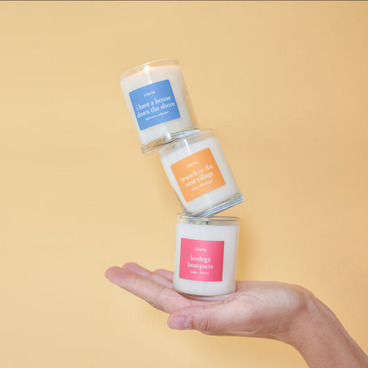 Three small candles balanced on a person's hand, each with different color labels and transparent containers.