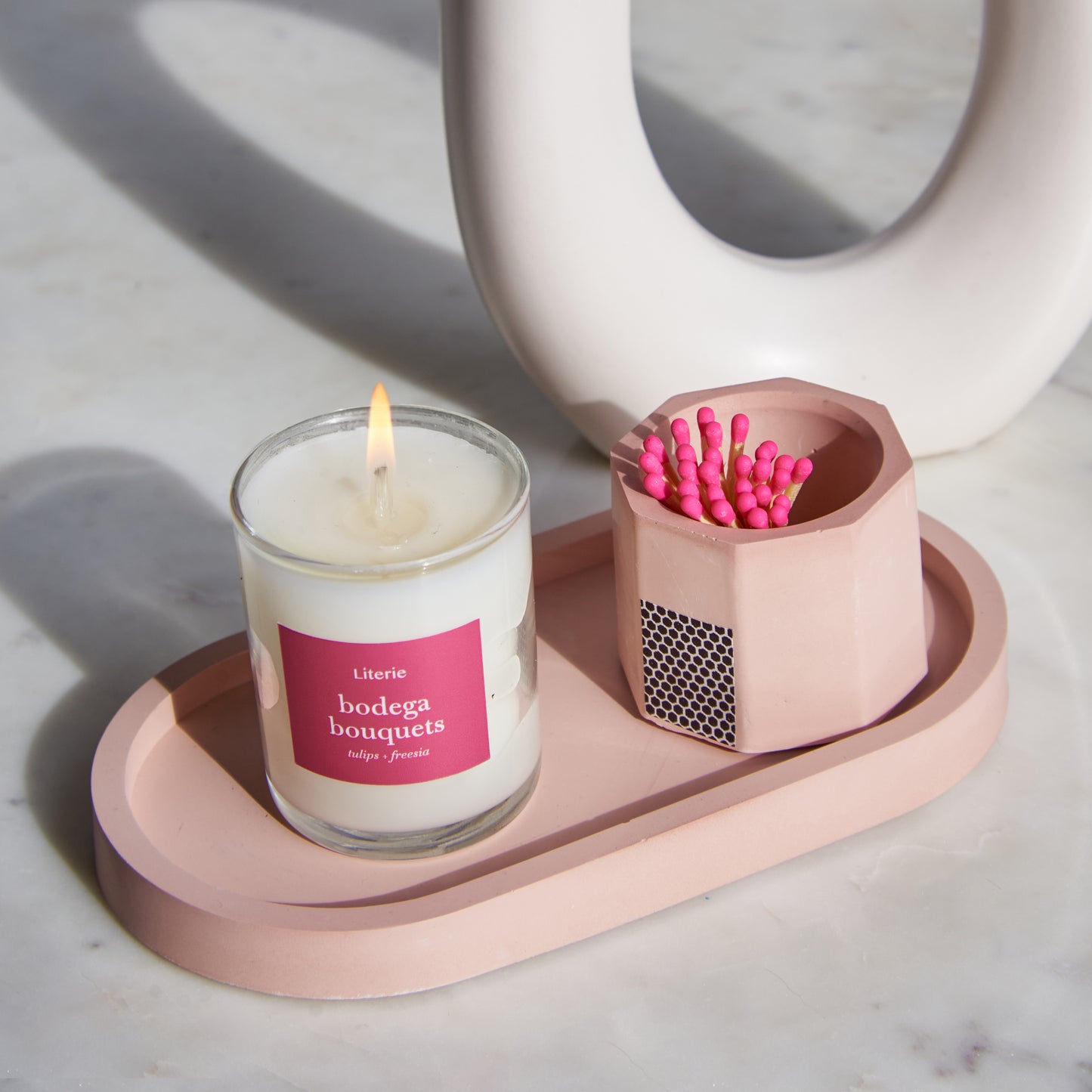 A pink concrete match holder with a hexagonal design and cork bottom, on a pink tray with a pink candle.