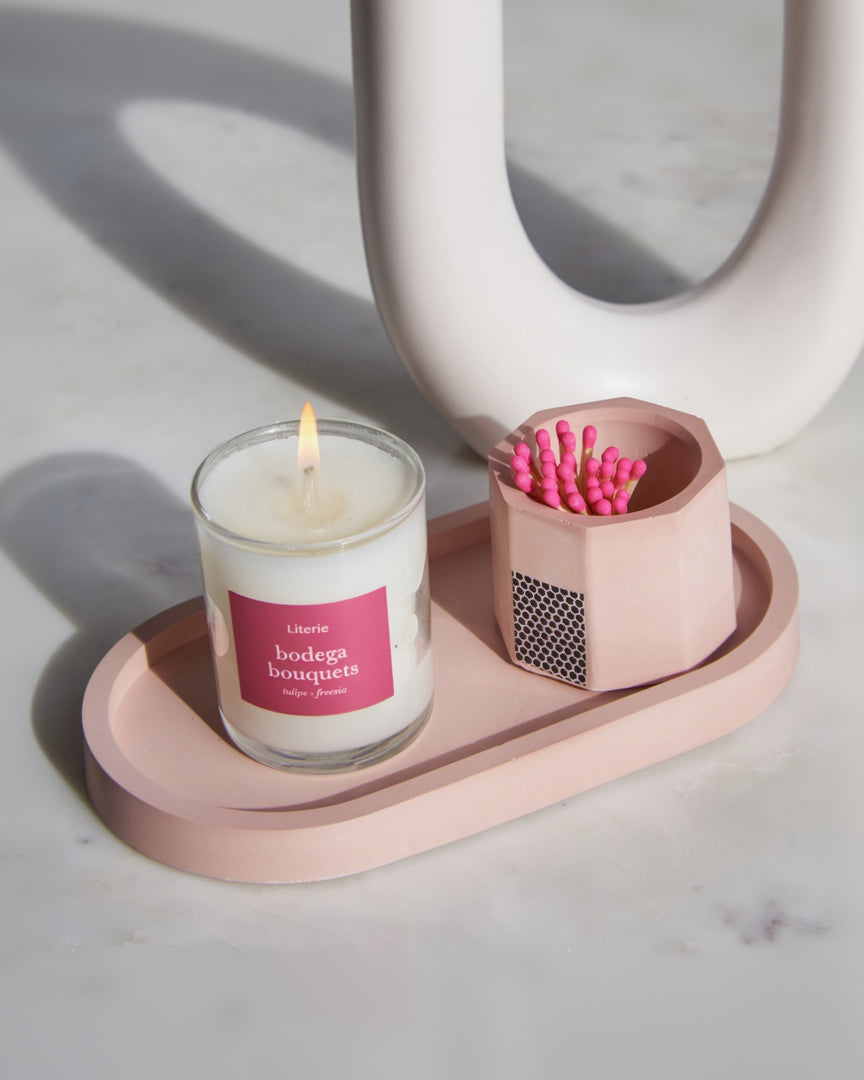 A pink concrete match holder with a hexagonal design and cork bottom, on a pink tray with a pink candle.