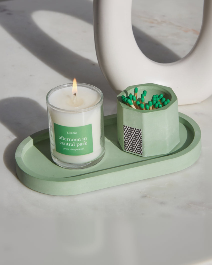 A green hand-poured concrete match holder with green matches and a candle on a green tray.