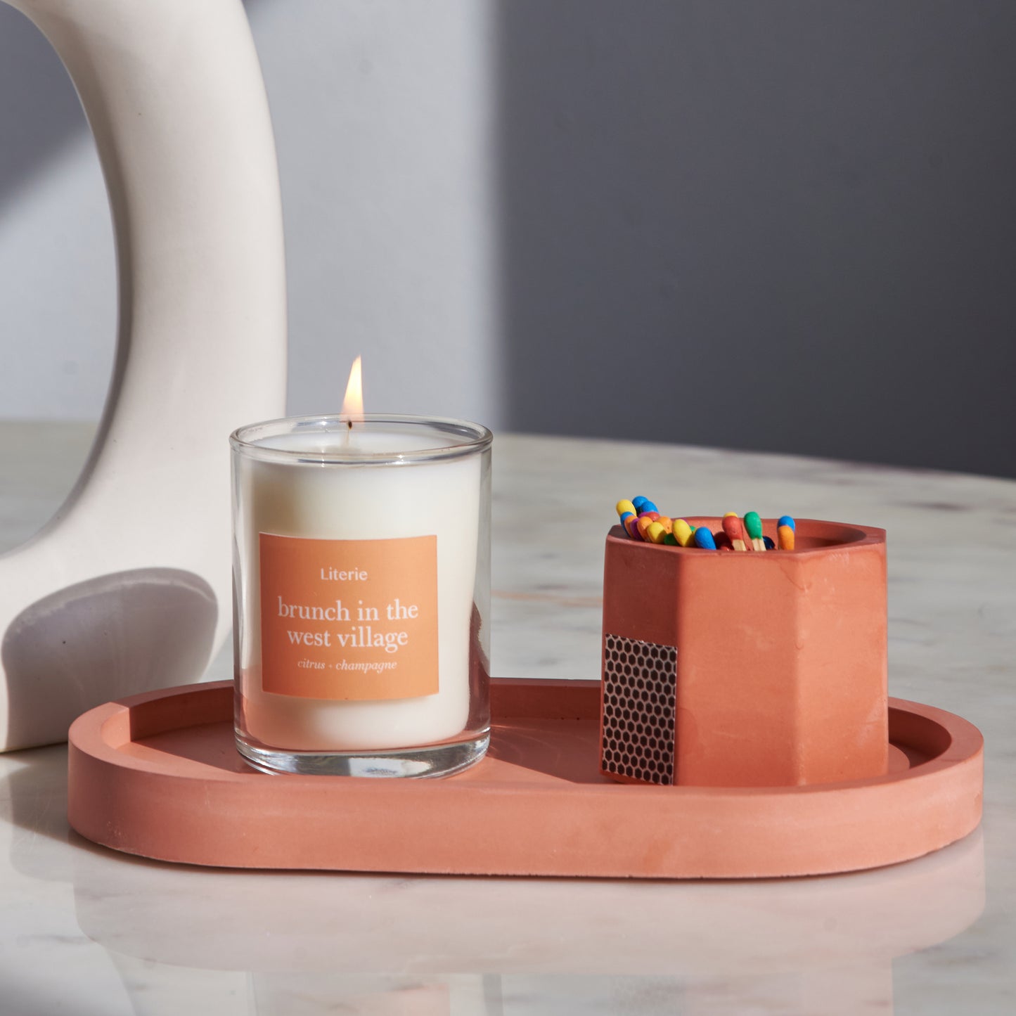 A orange concrete match holder with a hexagonal design on an orange tray with a candle.