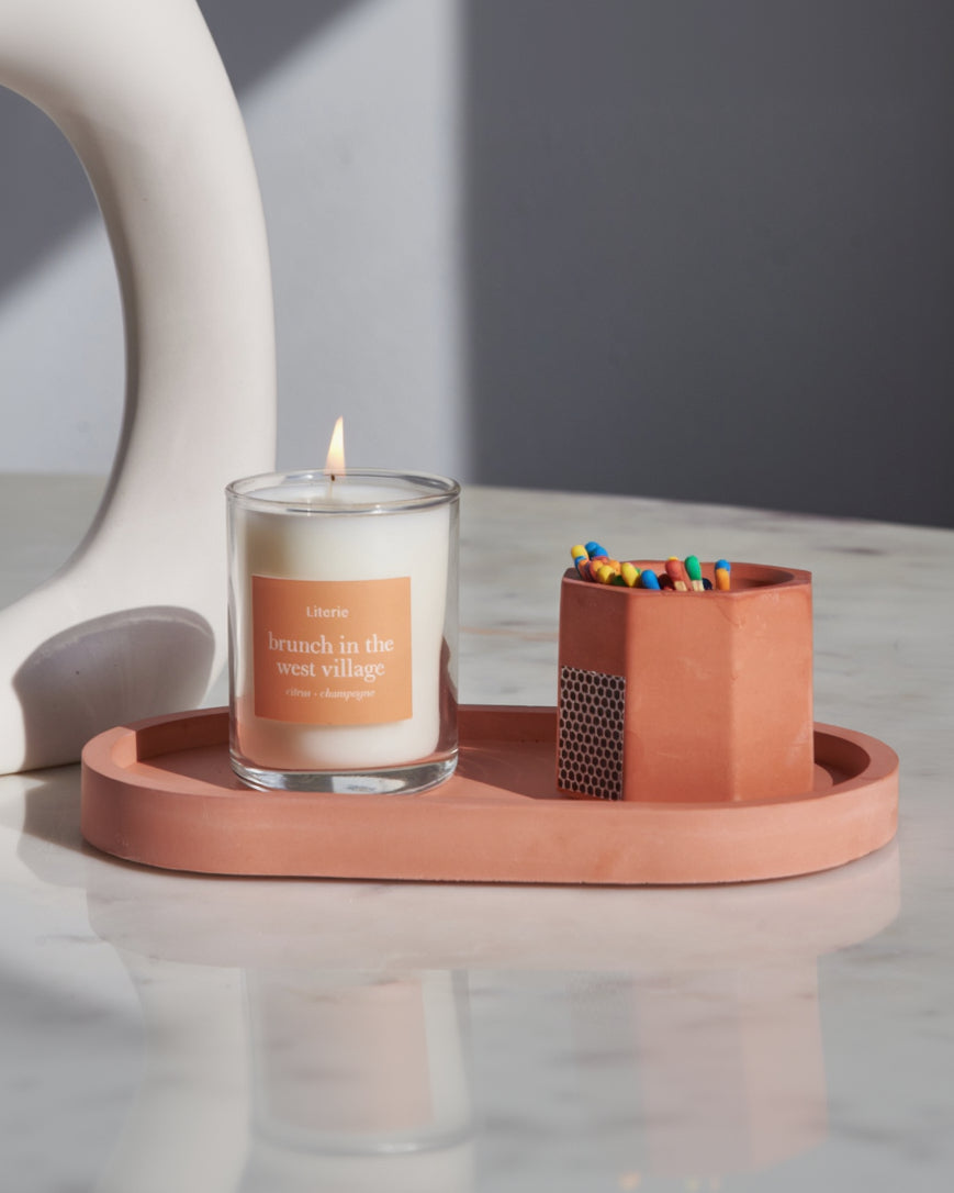 Brick colored pill shaped candle tray with orange candle and match sticks.