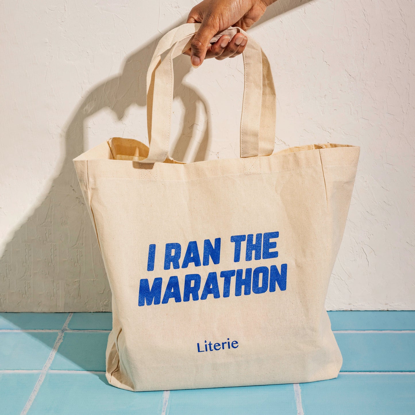 I Ran The Marathon canvas tote bag on blue tile.