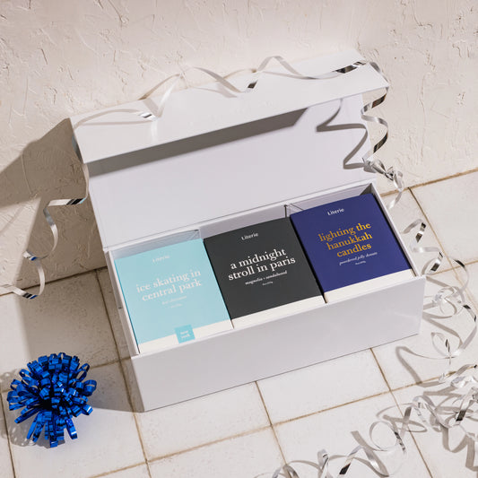 Set of three candles in a white gift box with ribbons on a tiled floor.