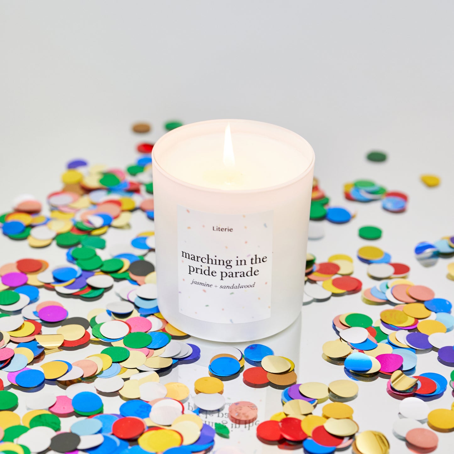 Candle with a label reading 'marching in the pride parade' surrounded by colorful confetti on a light background.