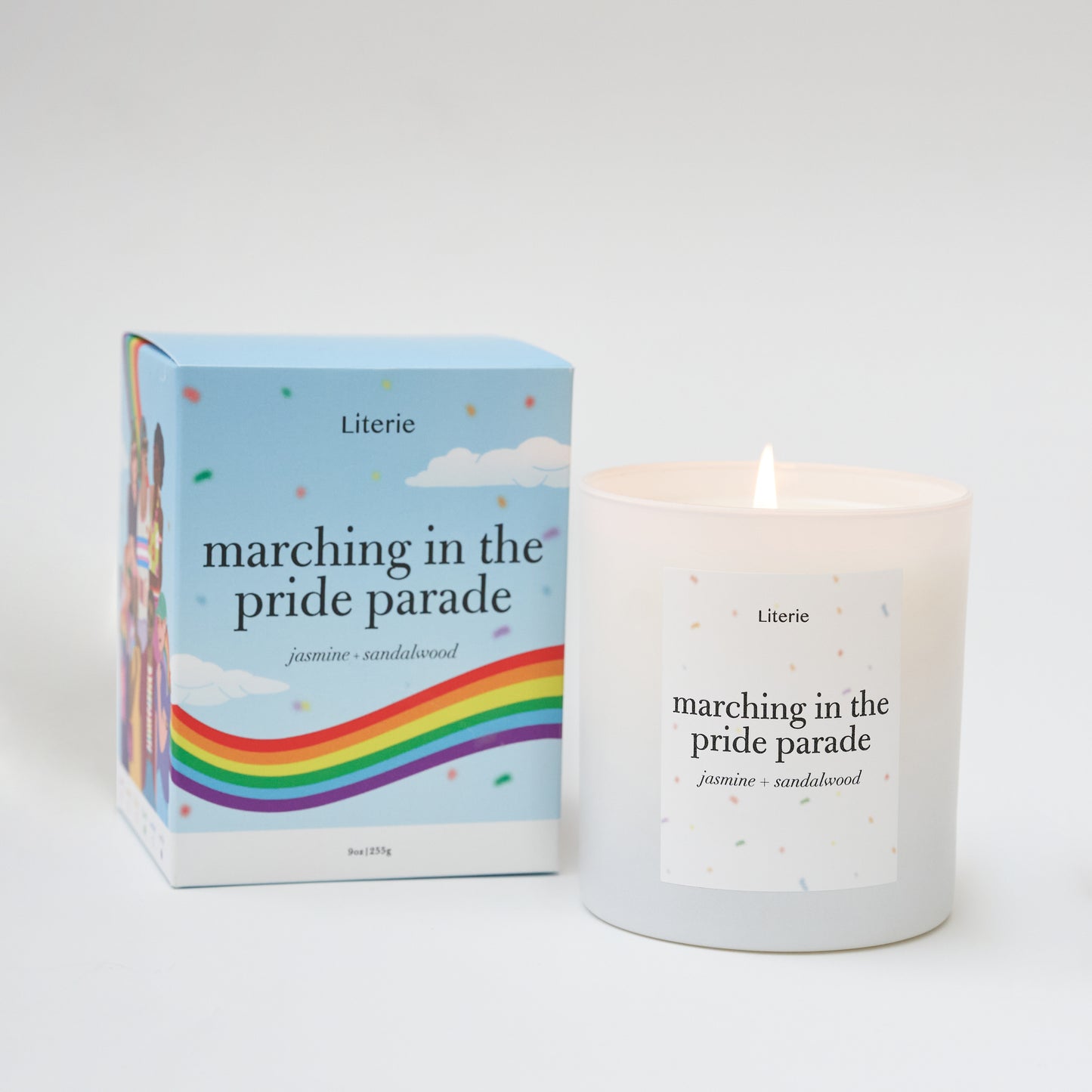 A white candle with text 'marching in the pride parade' on it, alongside a colorful box with rainbow stripes and the name 'Literie'.