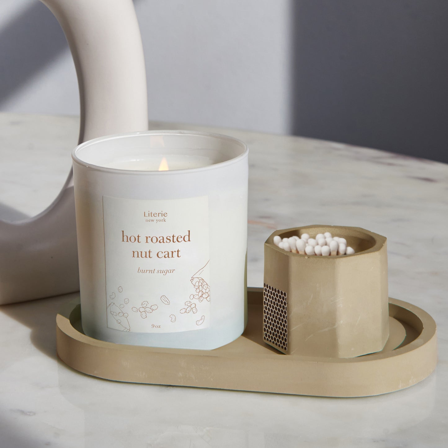 Taupe match stick holder with white matches on a tray with a candle.