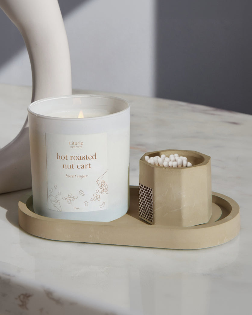 Taupe match stick holder with white matches on a tray with a candle.