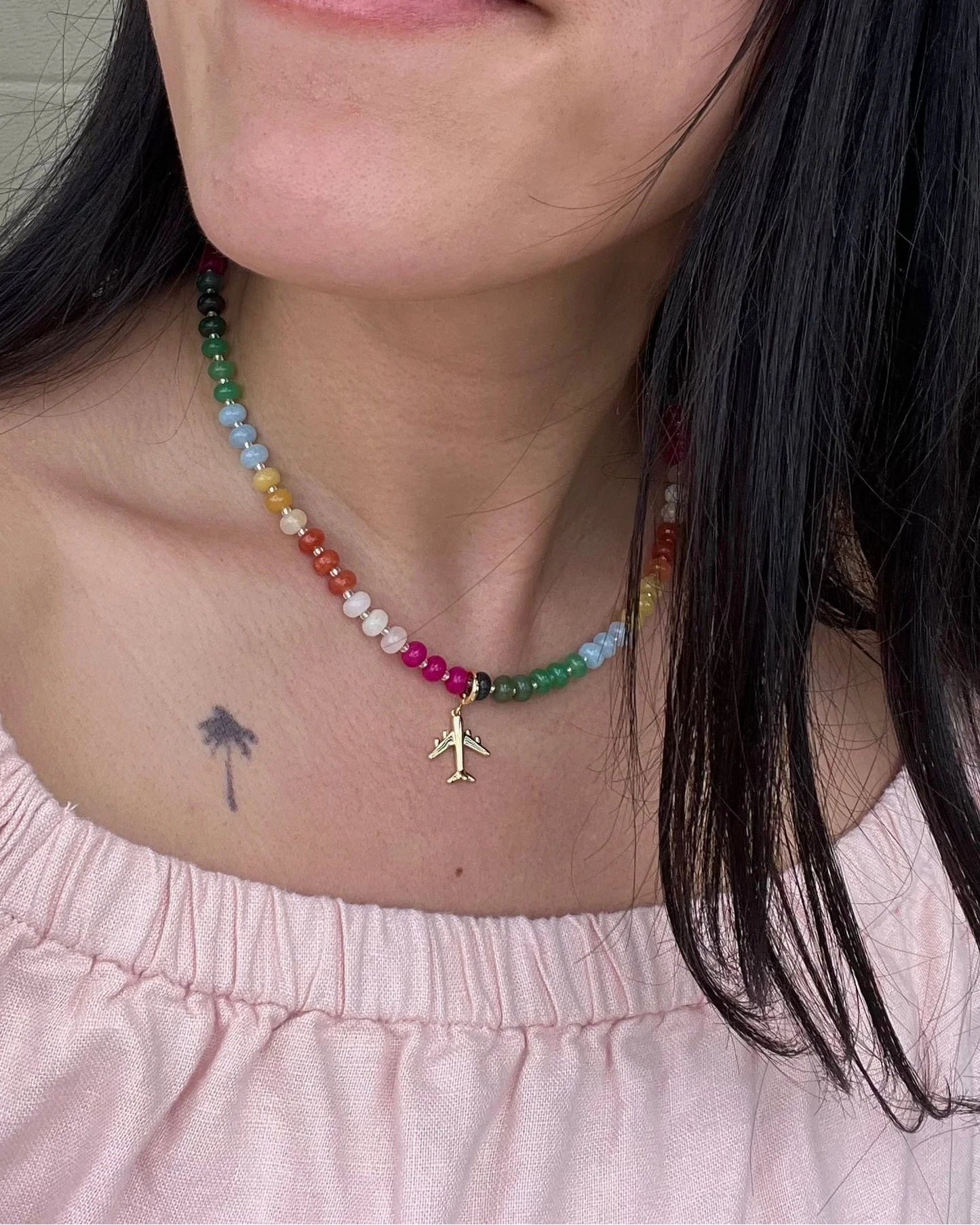 Close-up of a person wearing a colorful beaded necklace with a small airplane charm.