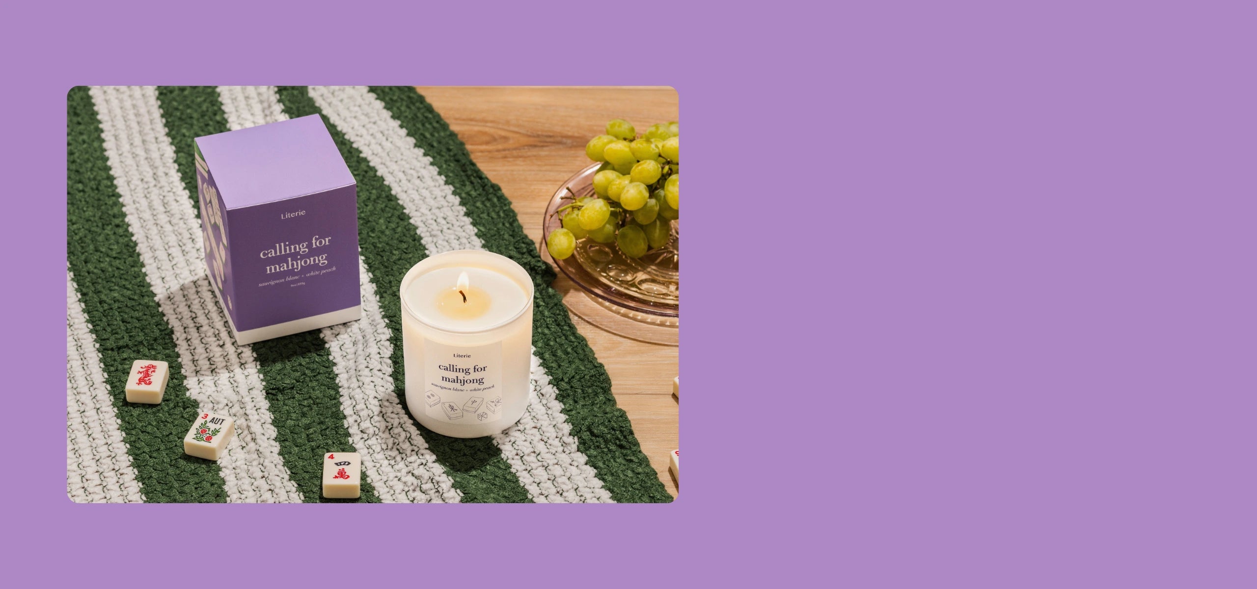 Calling for mahjong candle with packaging and grapes on a striped blanket.