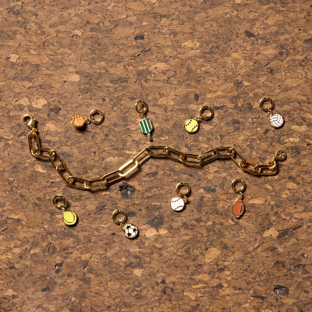 Gold chain bracelet with various charms on a cork surface