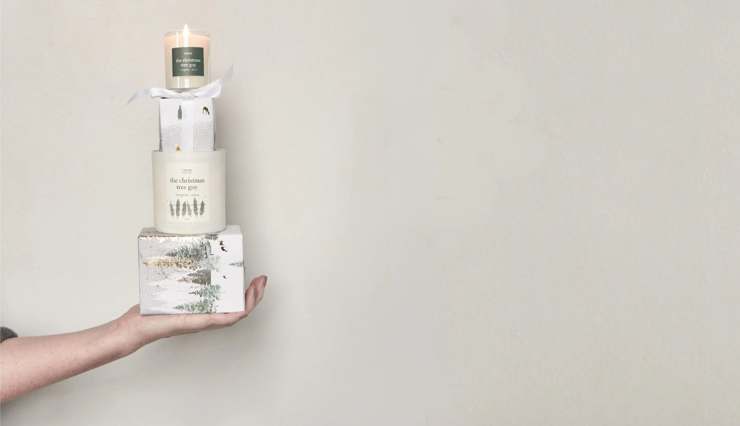 Hand holding a stack of candles and gifts against a plain background