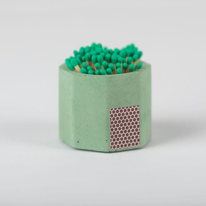 A green hand-poured concrete match holder with a cork bottom and green matches visible on top.