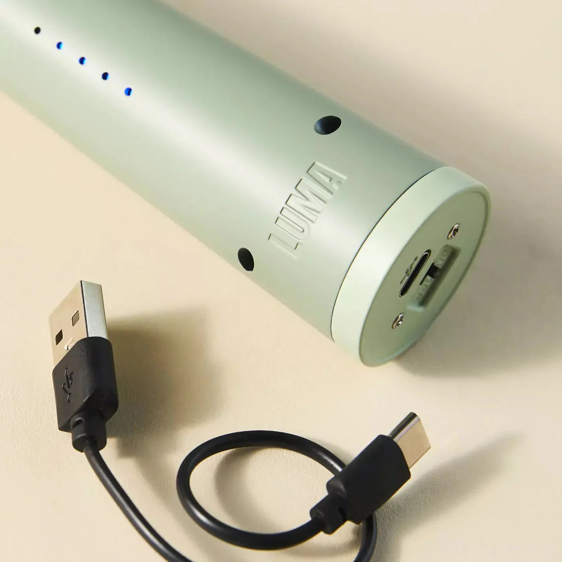 Light green lighter device with USB cable on a beige background.