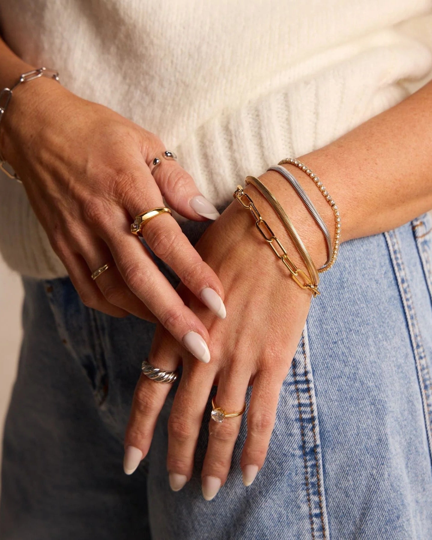 Close-up of hands with multiple bracelets and rings on a neutral background