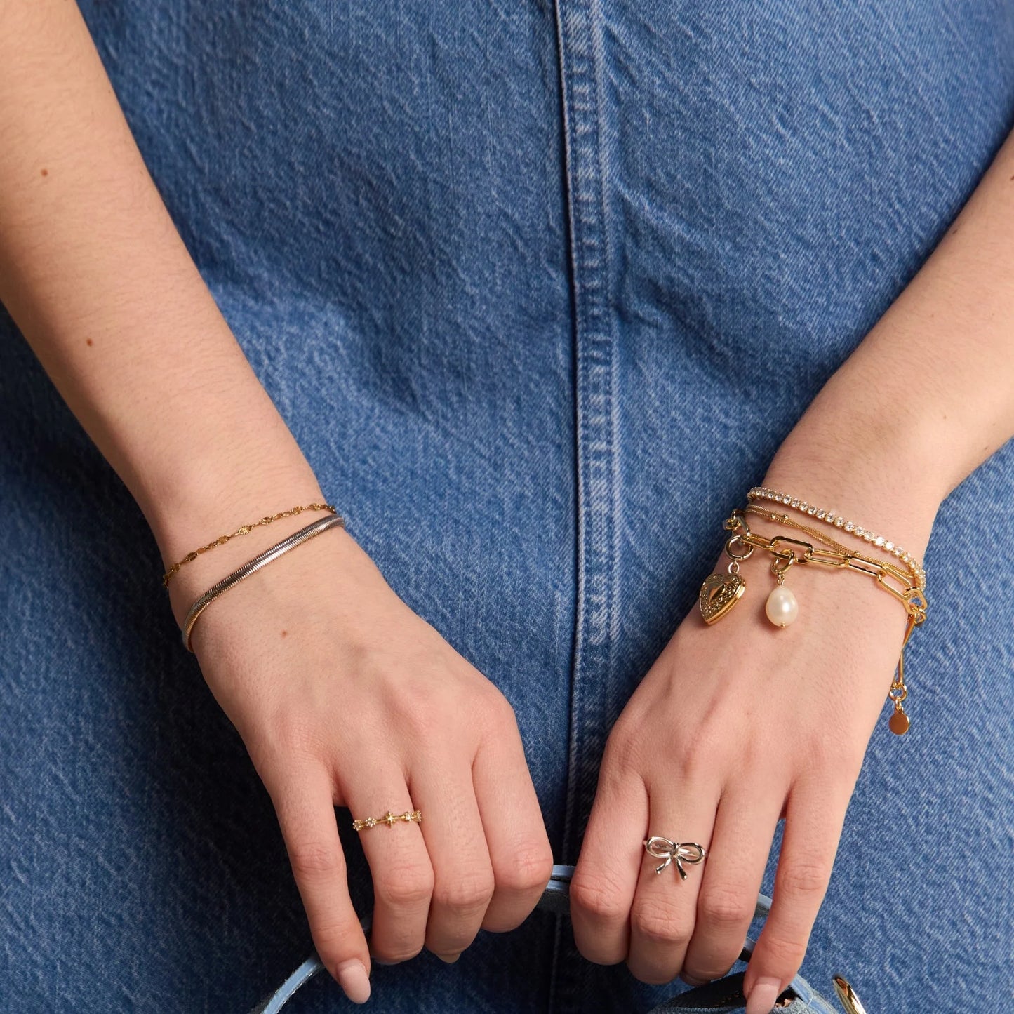 Real pearl charm to added to a bracelet stack on a wrist holding a purse.