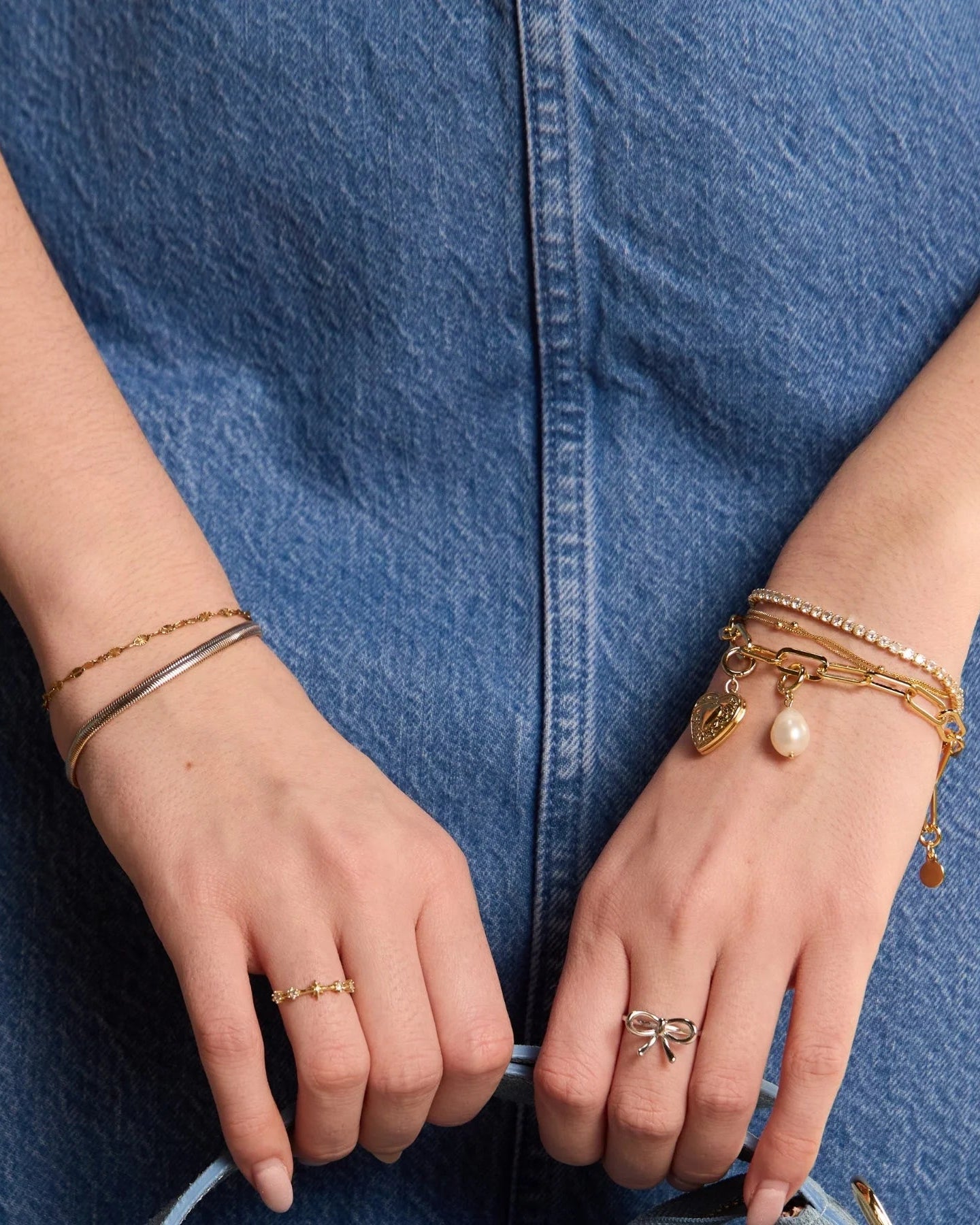 Real pearl charm to added to a bracelet stack on a wrist holding a purse.