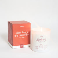 A candle with a label that reads 'pizza from a guy named joe' next to its packaging box which has similar text and a pizza slice illustration.