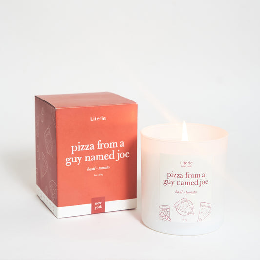 A candle with a label that reads 'pizza from a guy named joe' next to its packaging box which has similar text and a pizza slice illustration.