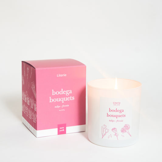 A candle with a label that reads 'bodega bouquets' next to its pink packaging box, also labeled with the same text.