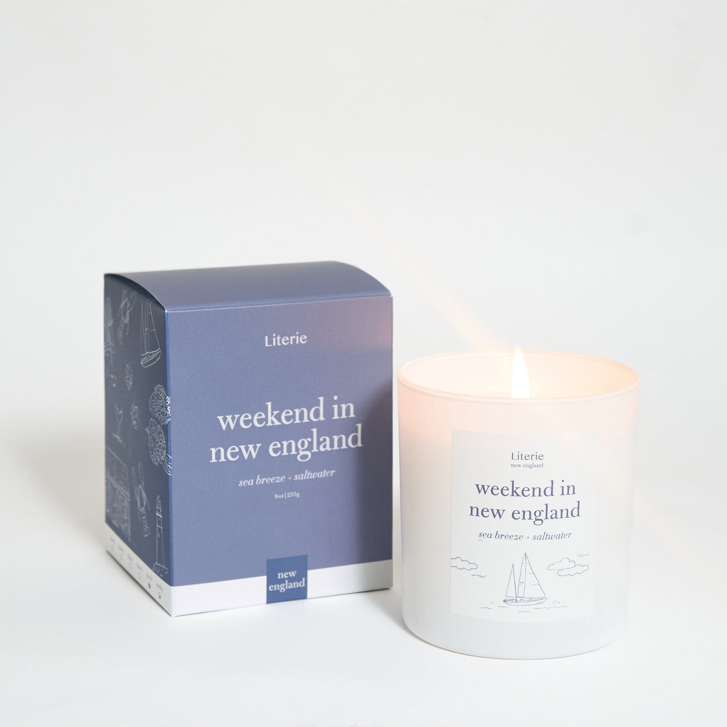 A scented candle with a label reading 'weekend in new england' alongside its packaging box which has similar text and design.