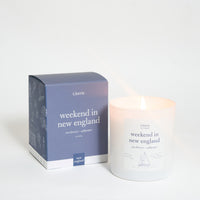 A scented candle with a label reading 'weekend in new england' alongside its packaging box which has similar text and design.