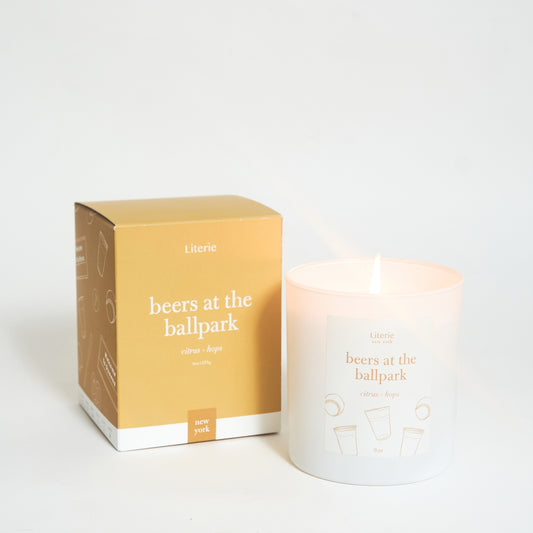 A candle with a label that reads 'Beers at the Ballpark' next to its packaging box which has similar design elements.