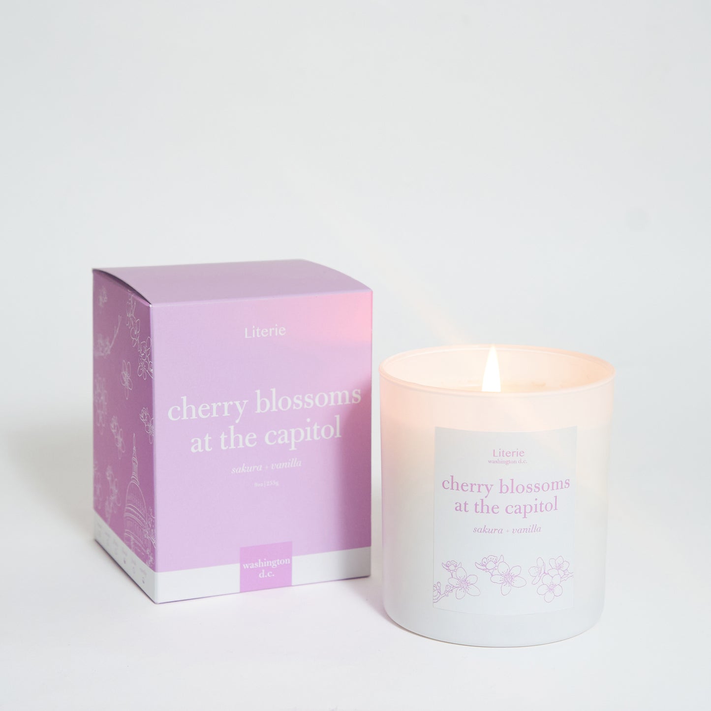 A scented candle with its packaging box, the candle is white and the box is pink with text and floral patterns.