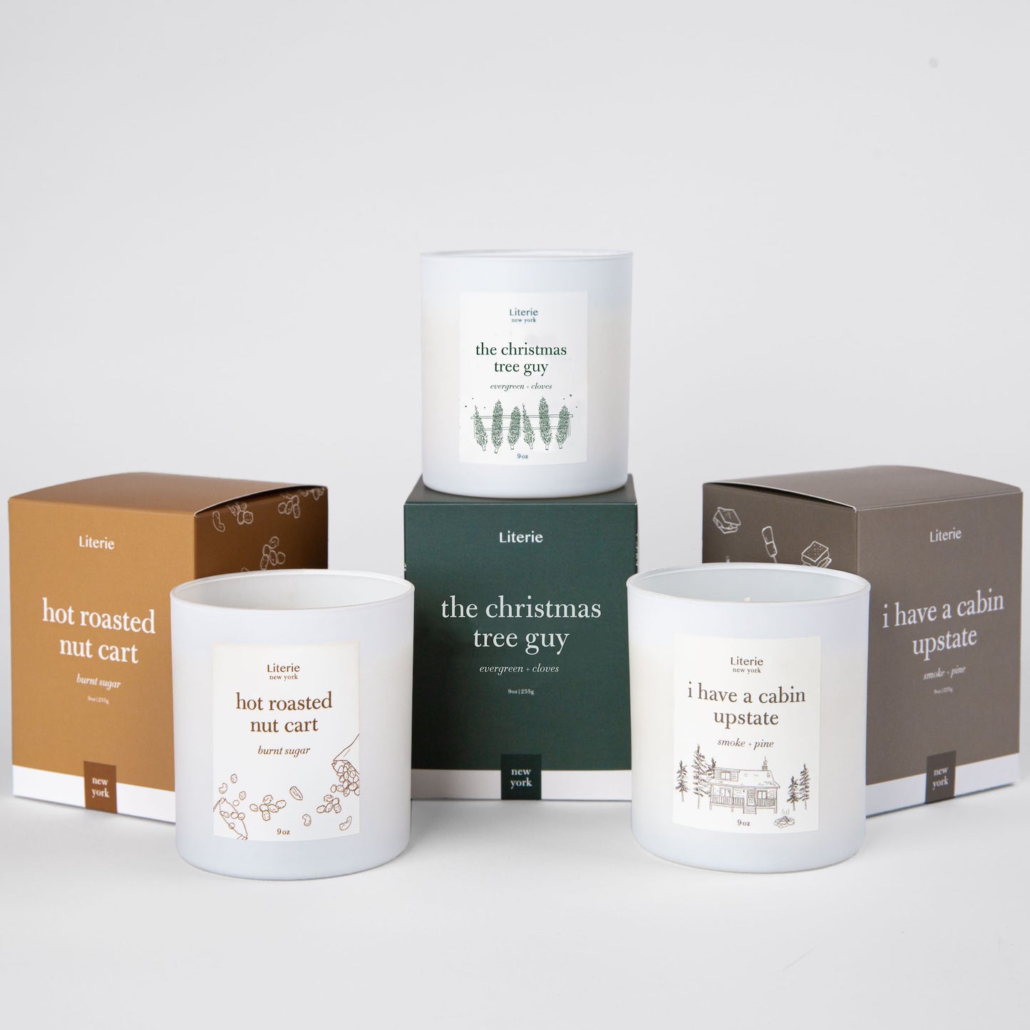Holiday gift box trio with three candles, nut cart, christmas tree, and cabin.