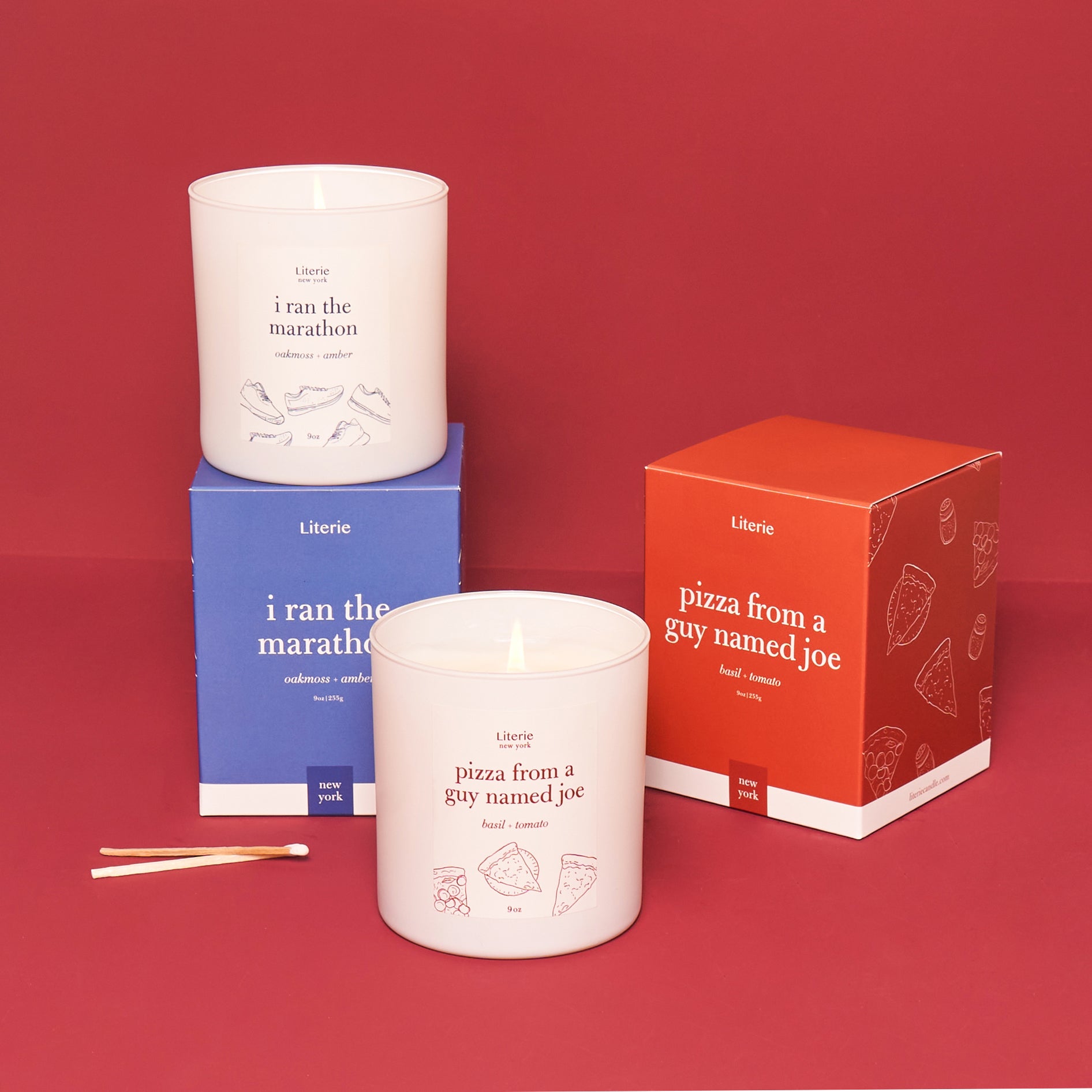 Two candles with labels 'i ran the marathon' and 'pizza from a guy named joe', along with their respective packaging boxes, on a red background.
