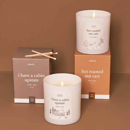 Two scented candles with packaging, one labeled 'i have a cabin upstate' and the other 'hot roasted nut cart'.