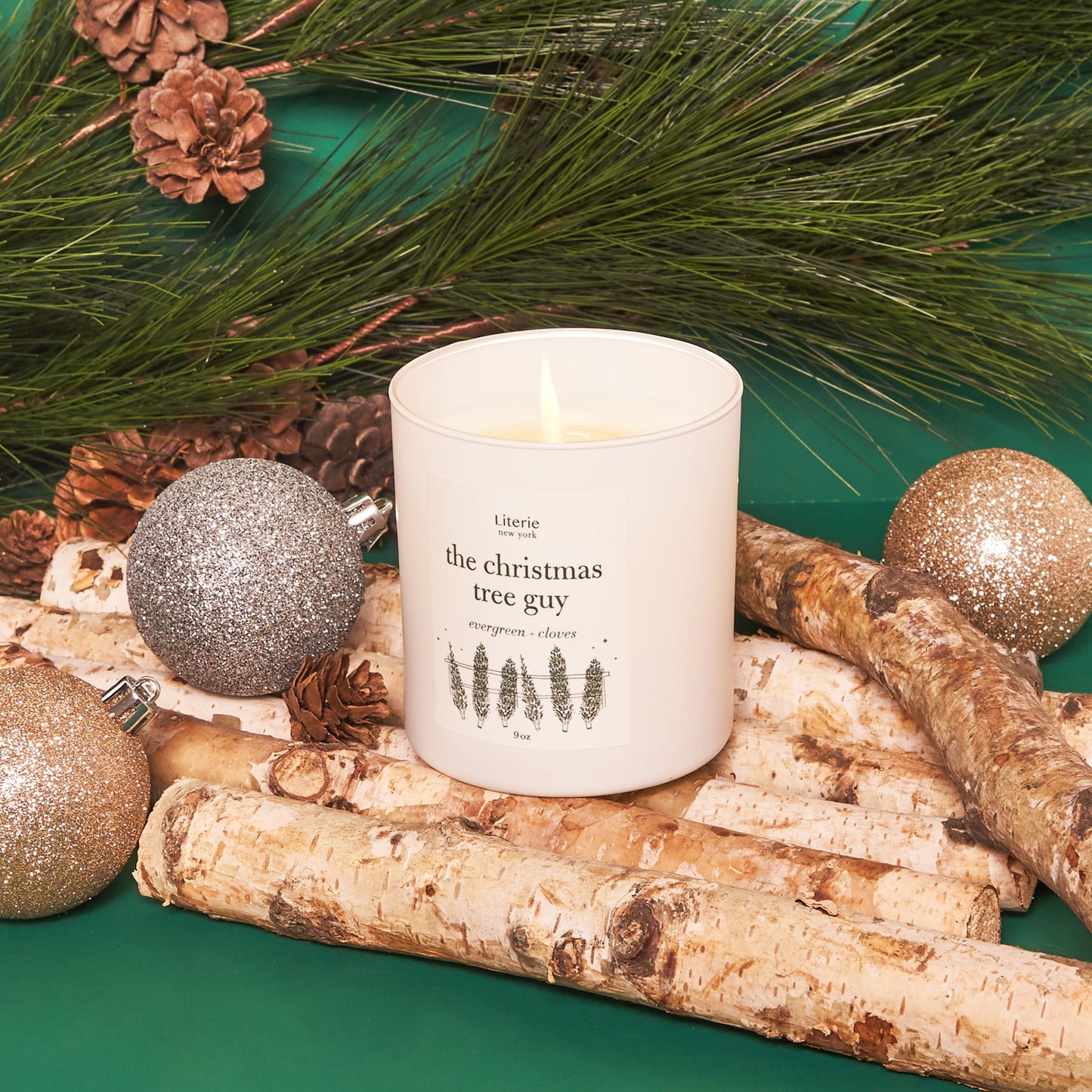 The Christmas Tree Guy candle next to ornaments.