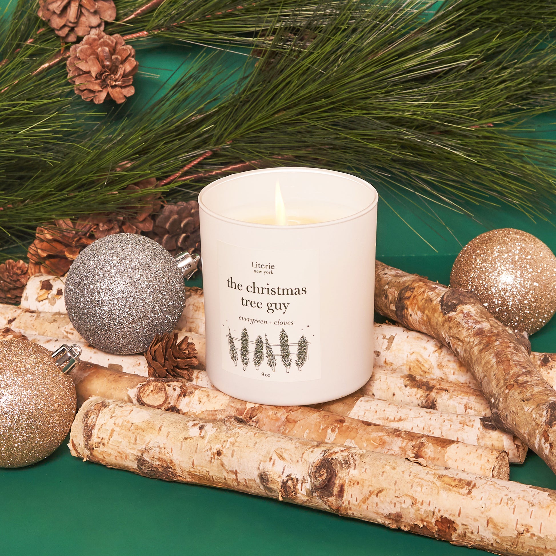 The Christmas Tree Guy candle next to ornaments.