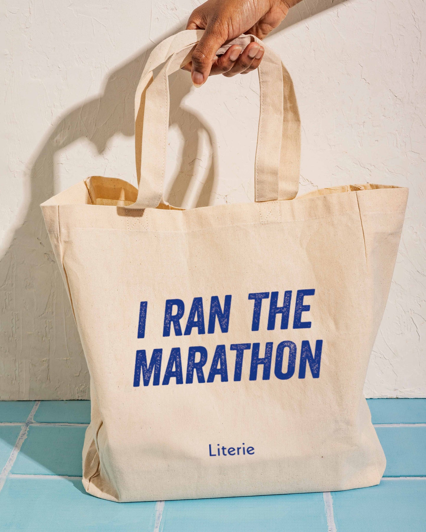 Beige tote bag with 'I Ran The Marathon' text and 'Literie' branding on a light background.