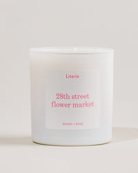 White candle with a '28th street flower market' label on a light gray background