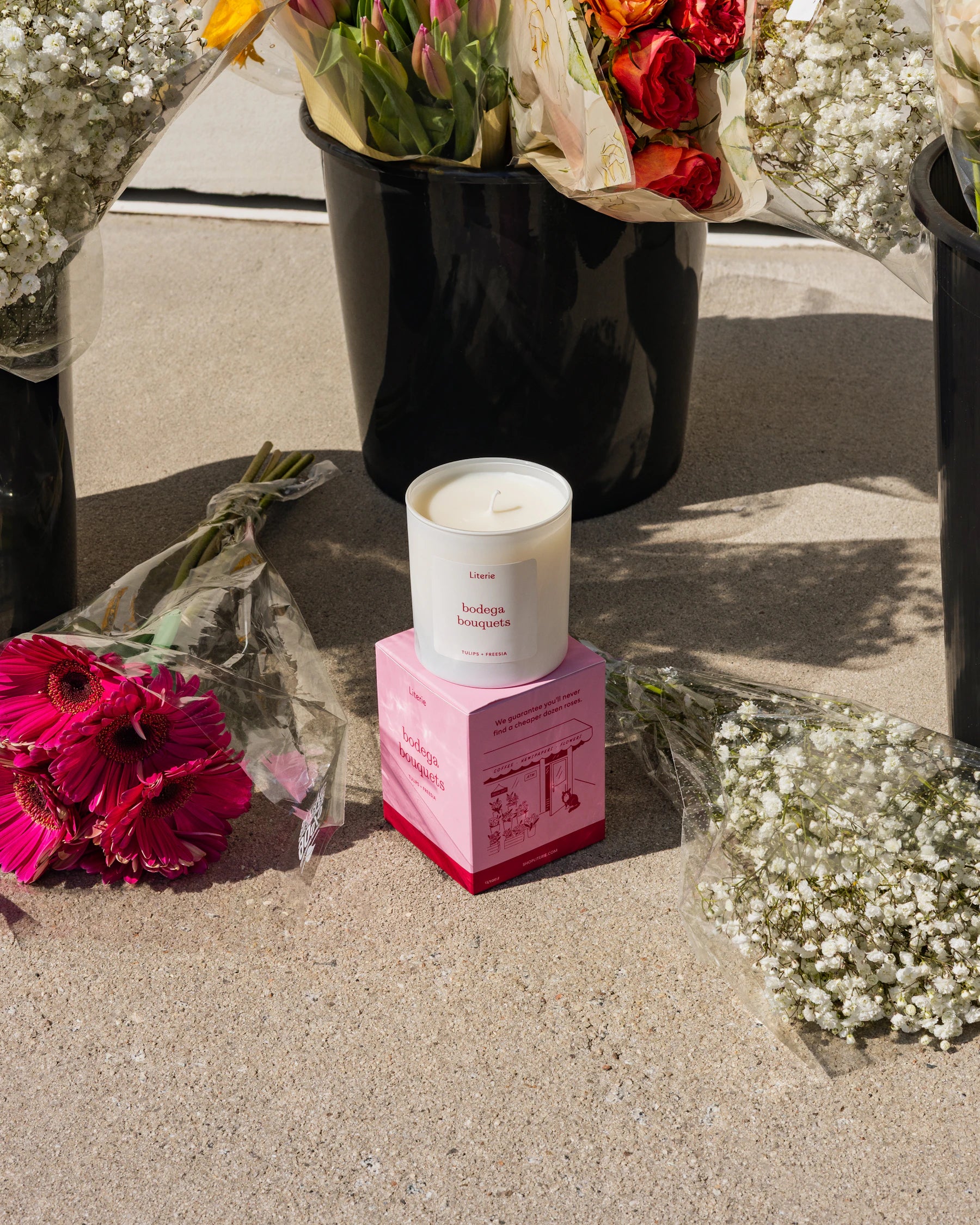 Bodega Bouquets floral scented candle on it's pink box with flowers in the background.