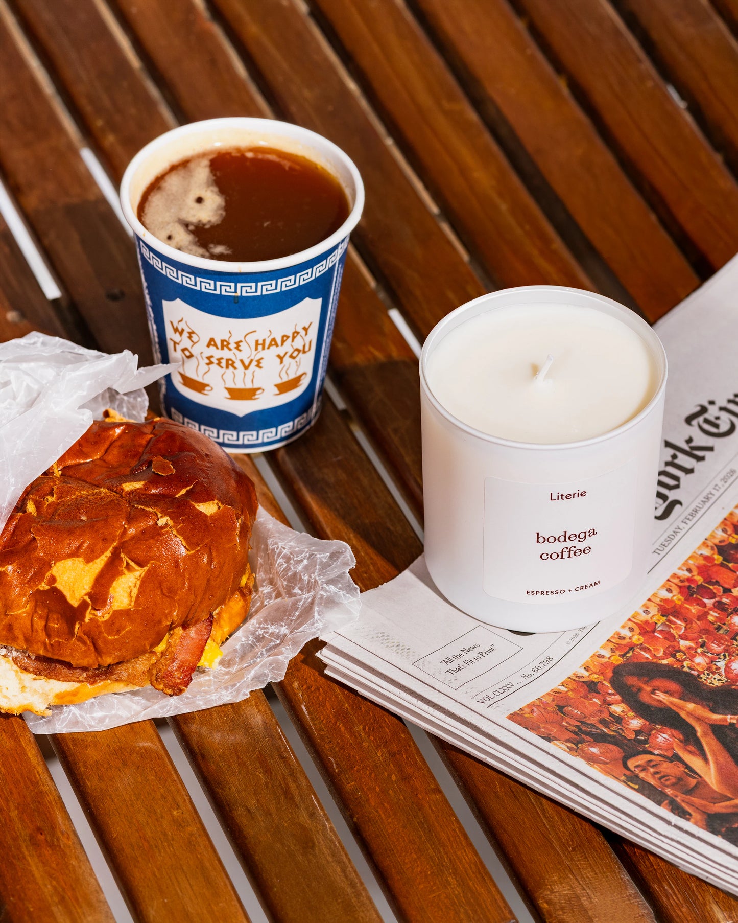 Literie's "bodega coffee" candle next to a bacon, egg, and cheese and a cup of coffee.