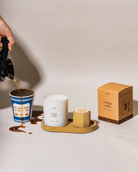 Person pouring coffee into a cup with a 'bodega coffee' candle on a tray with matches.