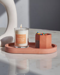 A orange concrete match holder with a hexagonal design on an orange tray with a candle.