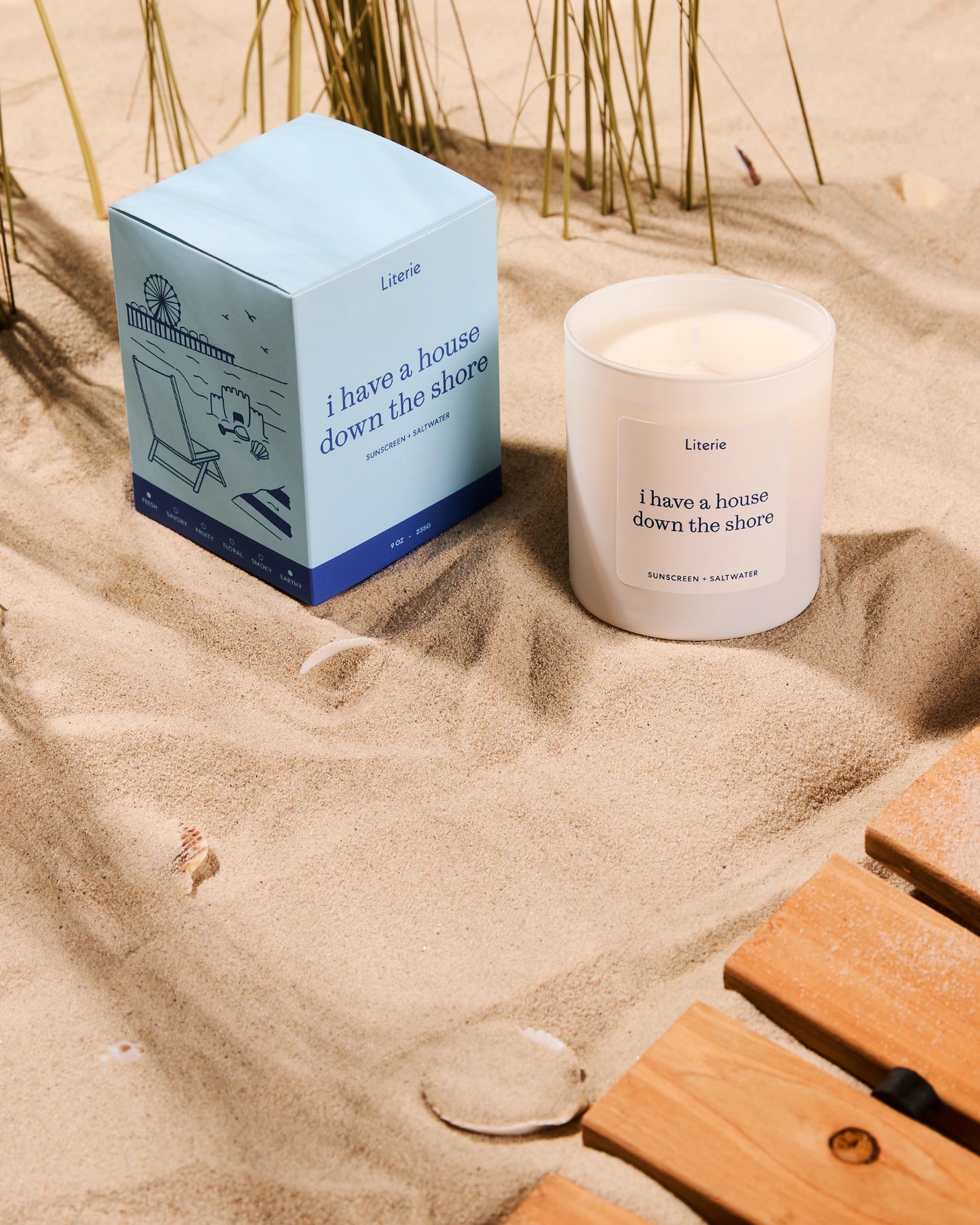 'i have a house down the shore' candle with box in the sand surrounded by seashells.