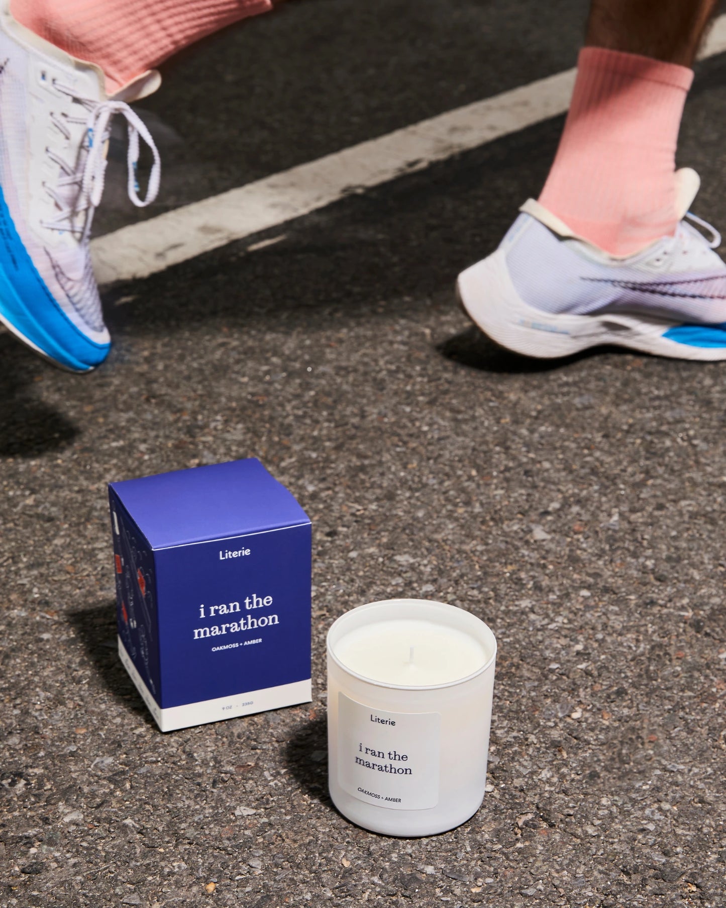 Candle and packaging labeled 'I ran the marathon' on a road with running shoes in the background.