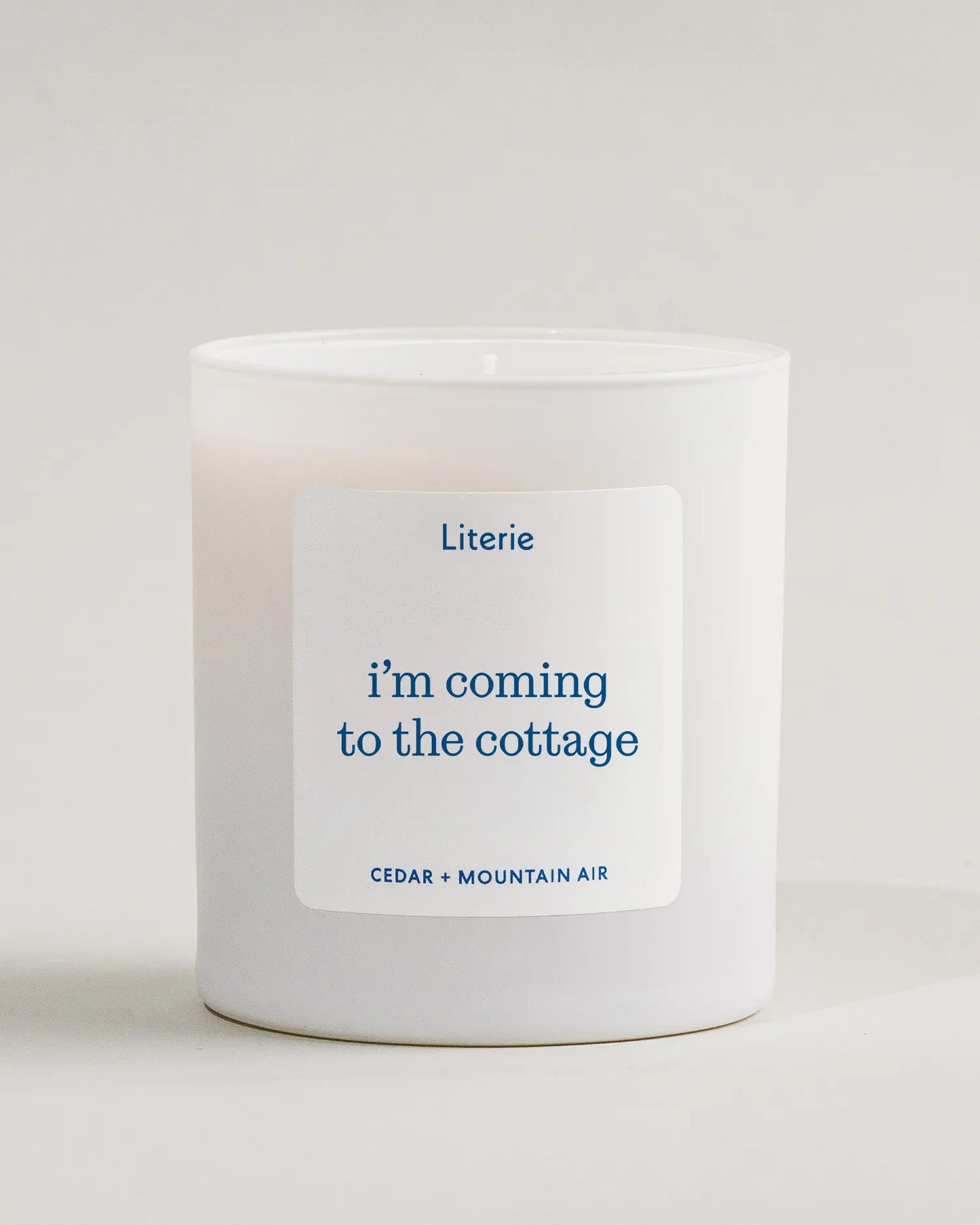 White candle with a 'i'm coming to the cottage' candle label on a light gray background inspired by the show 'Heated Rivalry'.
