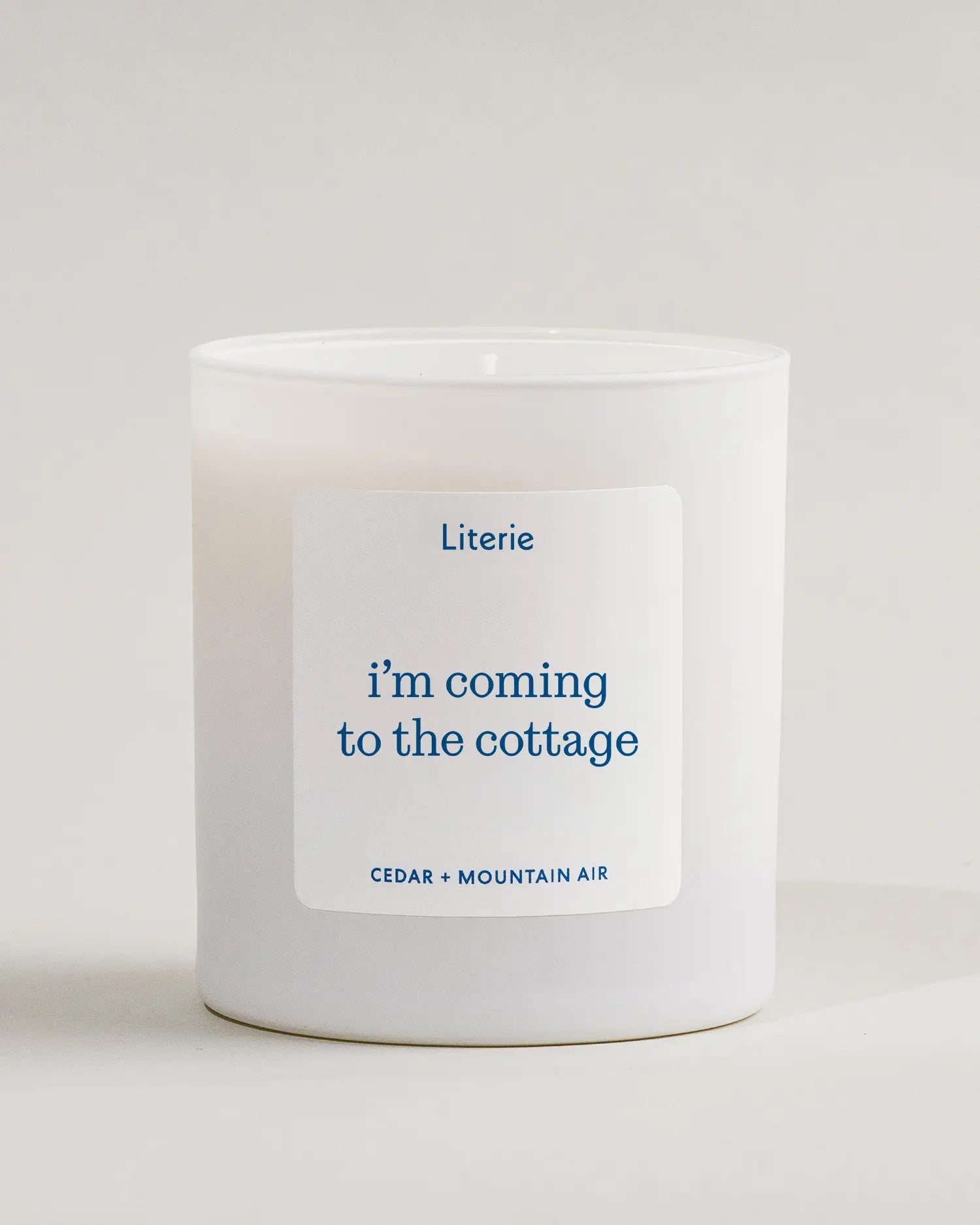 White candle with a 'i'm coming to the cottage' candle label on a light gray background inspired by the show 'Heated Rivalry'.