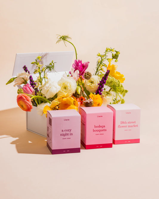 "a cozy night in", "bodega bouquets", and "28th street flower market" candles in front of their white gift box with florals popping out.