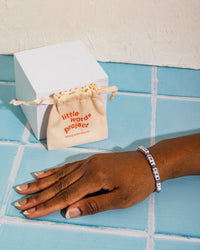 Hand with 'i ran the marathon' bracelet and small beige bag labeled 'little words project'.