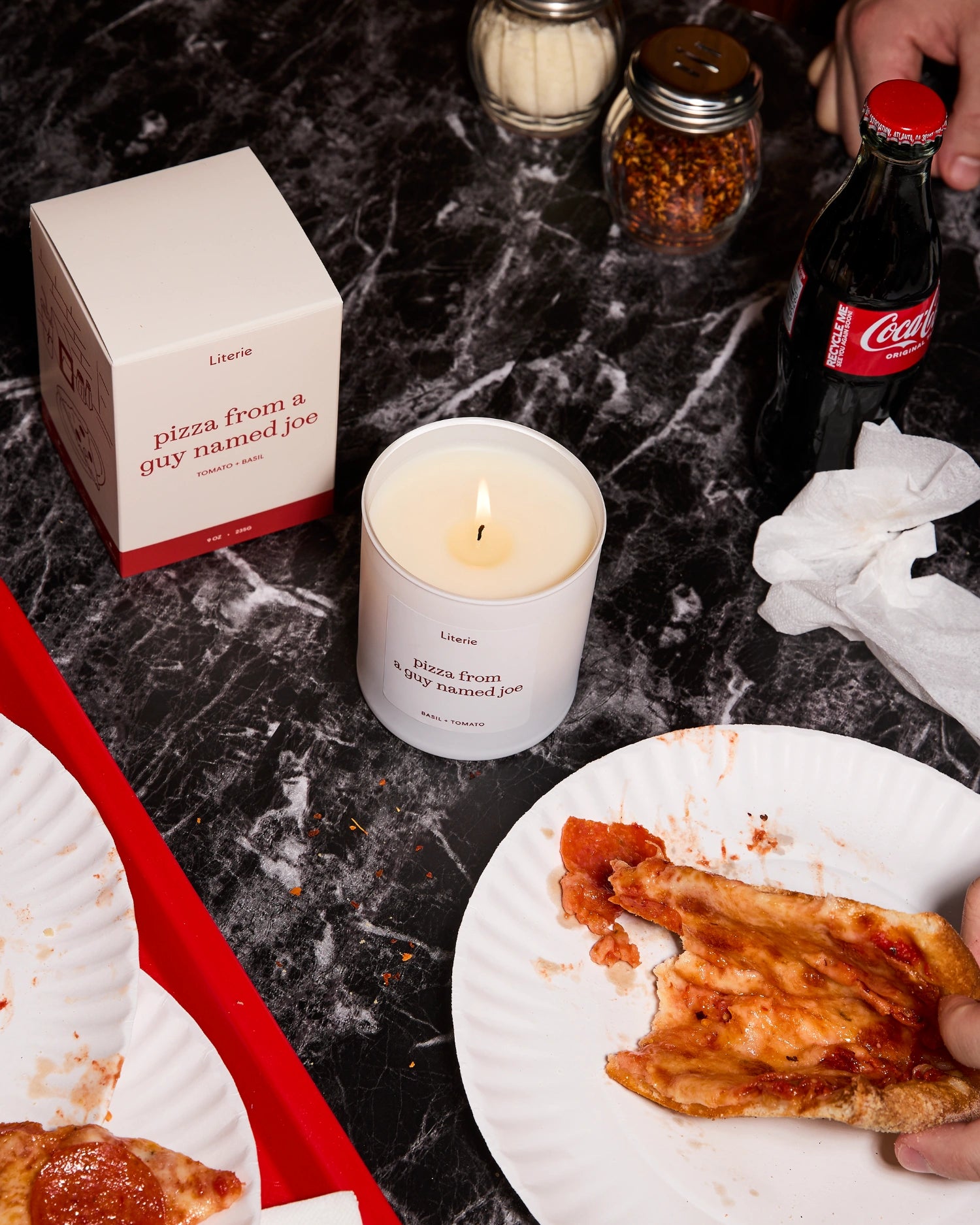 'Pizza from a guy named Joe' candle on a marble surface with pizza slices and a soda bottle.