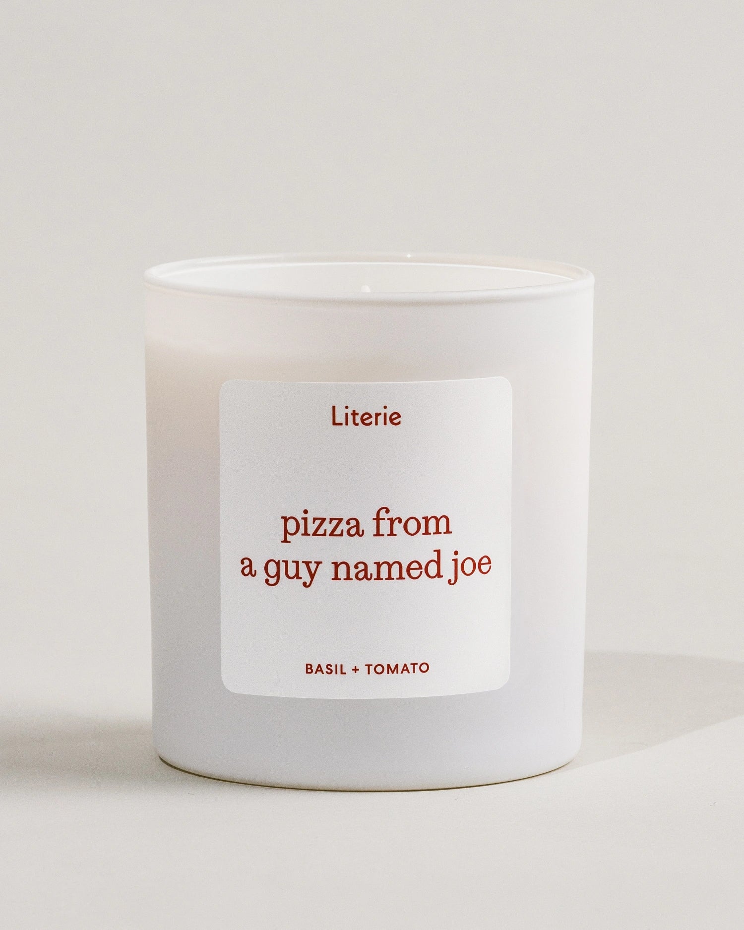 White Literie candle with a label reading 'pizza from a guy named Joe' on a light background