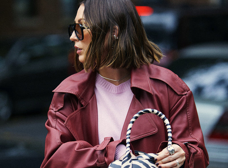Woman in a red jacket holding a zebra-striped handbag on a city street.