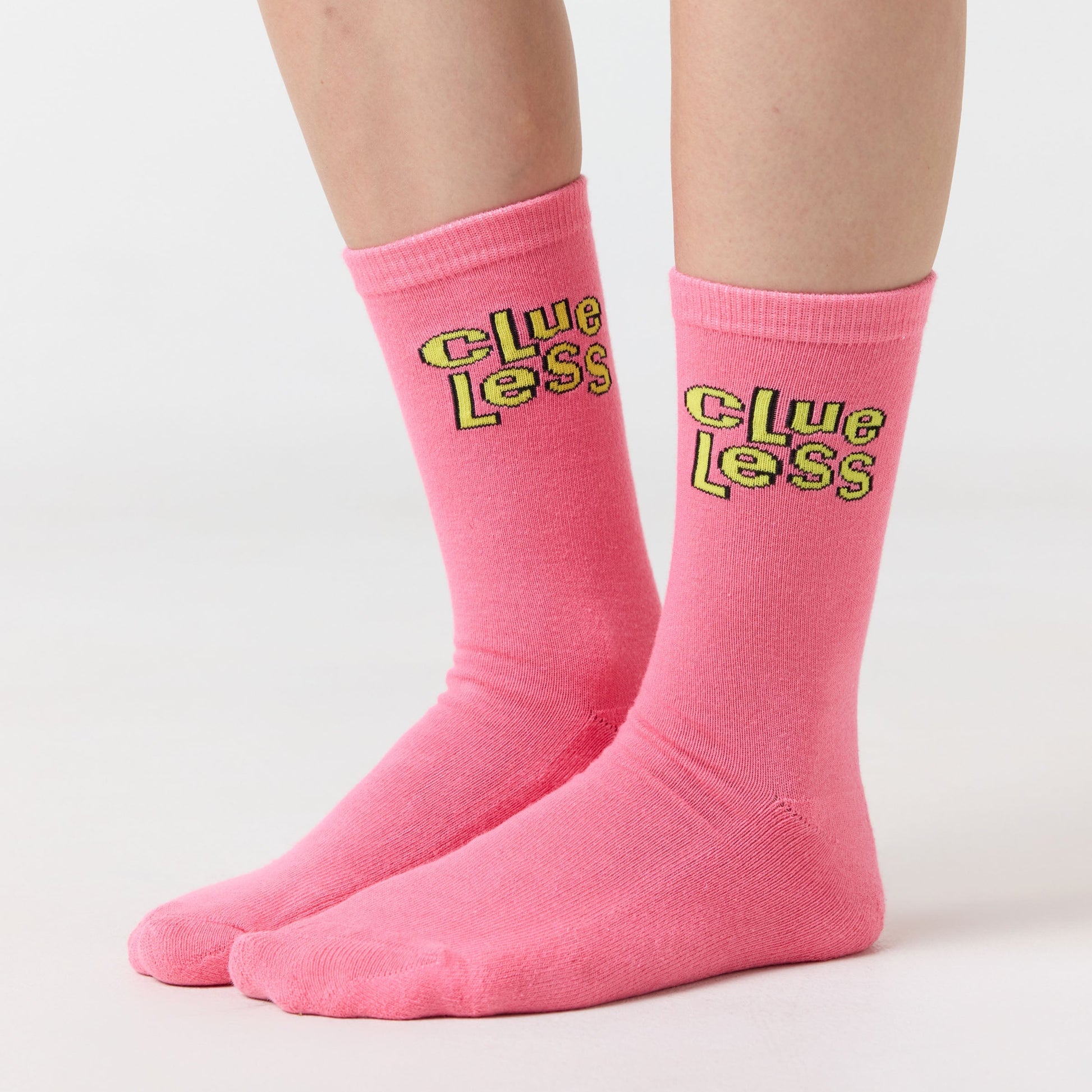 Pink socks with yellow text 'Clueless' worn by a person on a light gray background